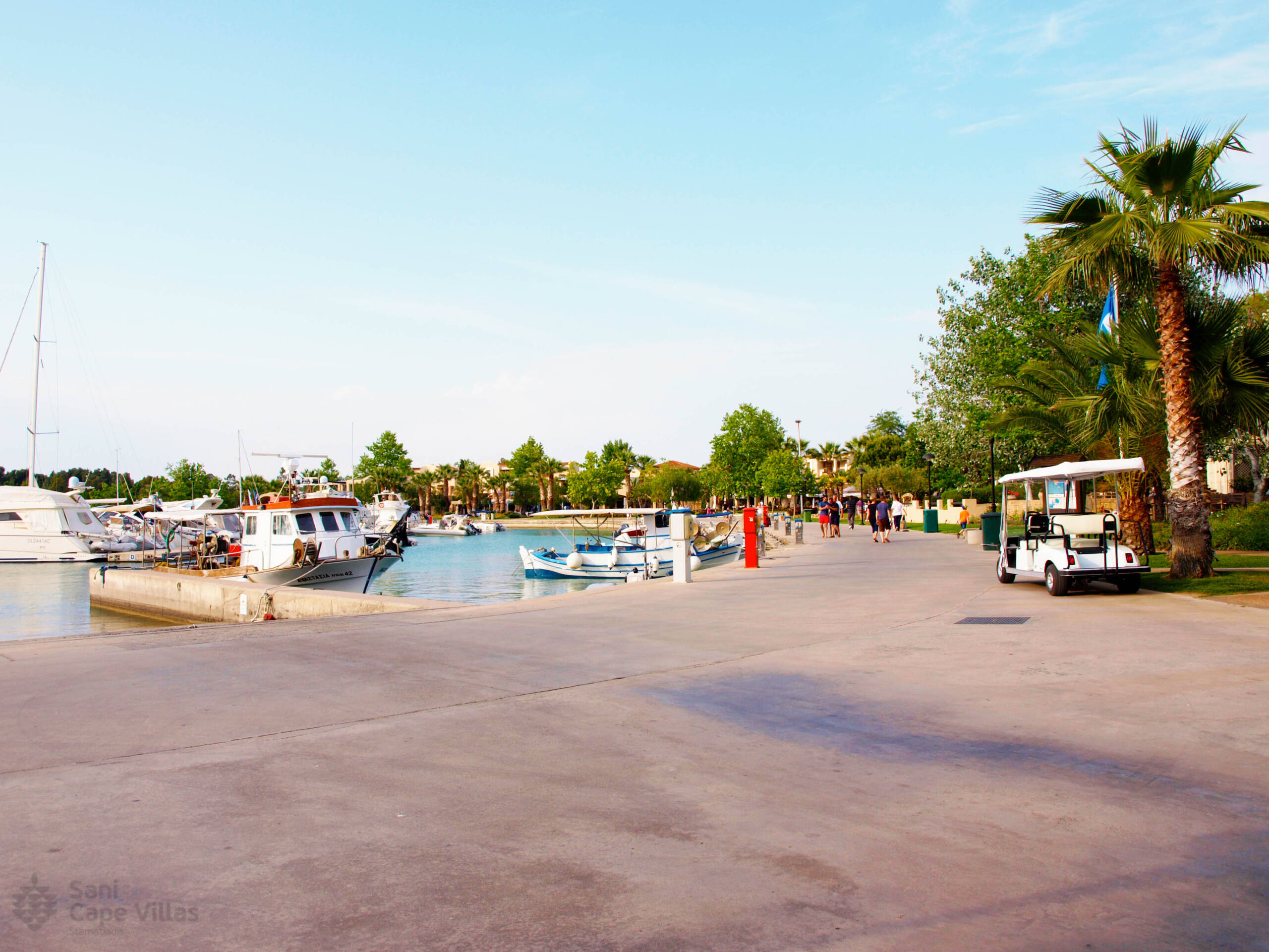 Sani Marina with moored boats, people walking the promenade and palm trees are located along the way